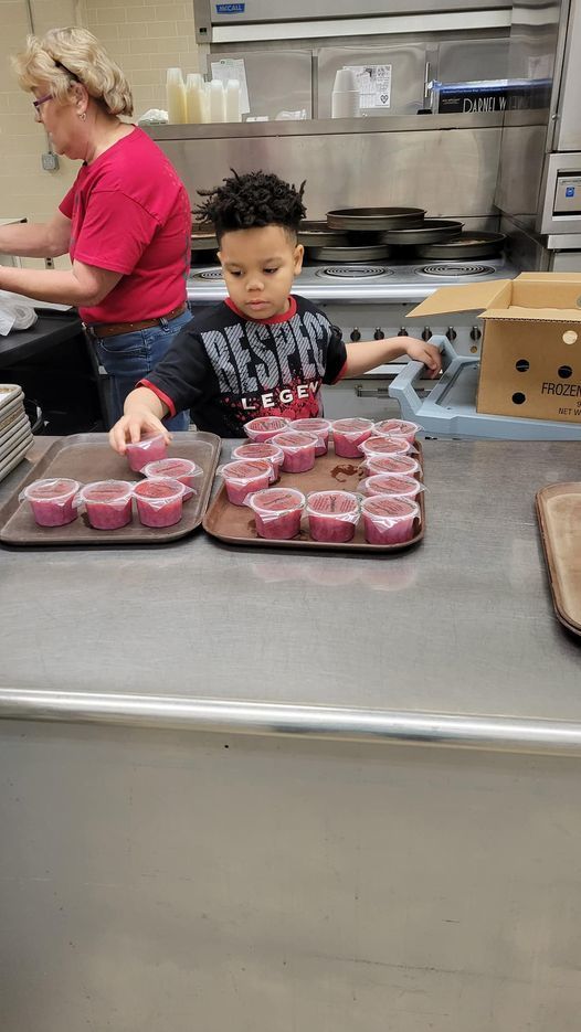 Little boy helps lay out jello cups in kitchen
